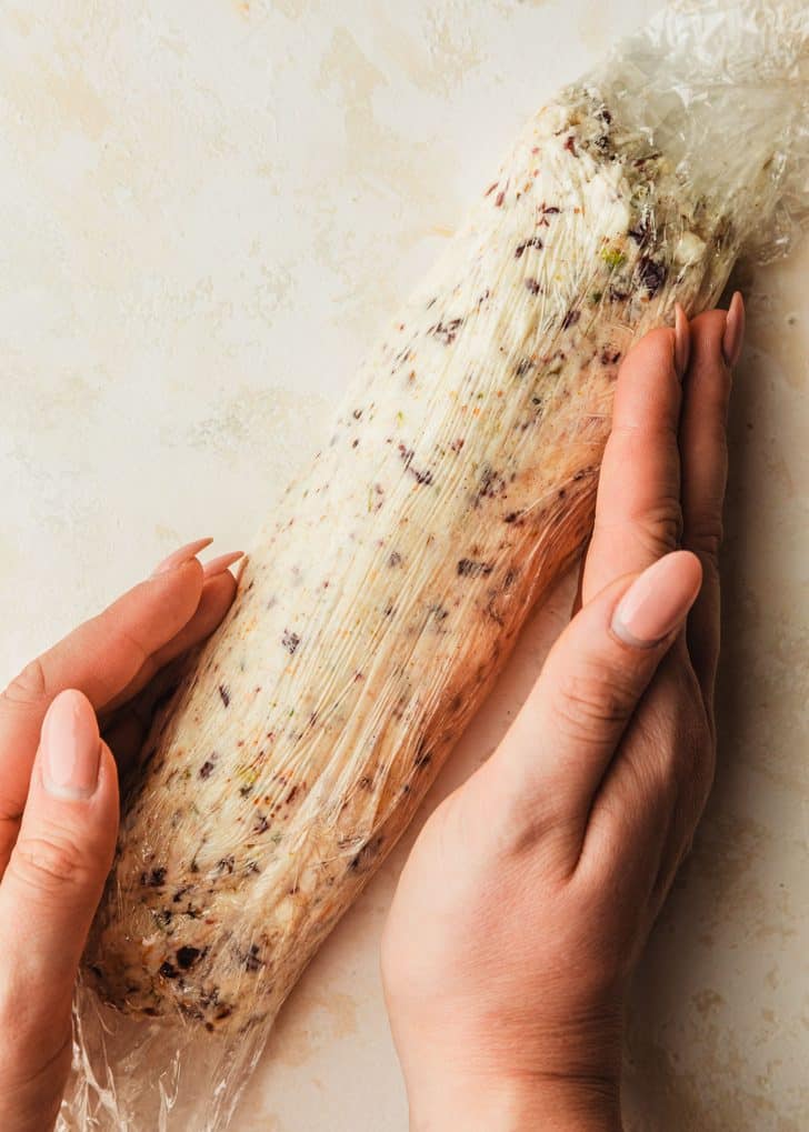 Hands shaping cheese in plastic wrap.