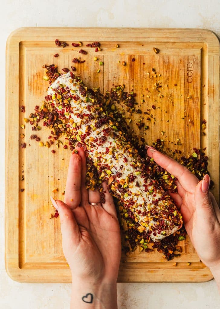 Hands forming a cranberry feta cheese log on a wood board.