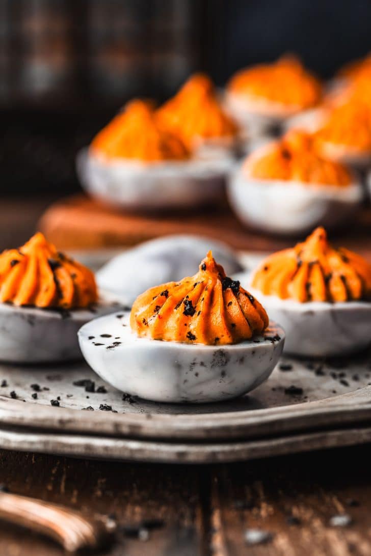 A silver plate and wooden board of Halloween deviled eggs on a rustic wooden counter.