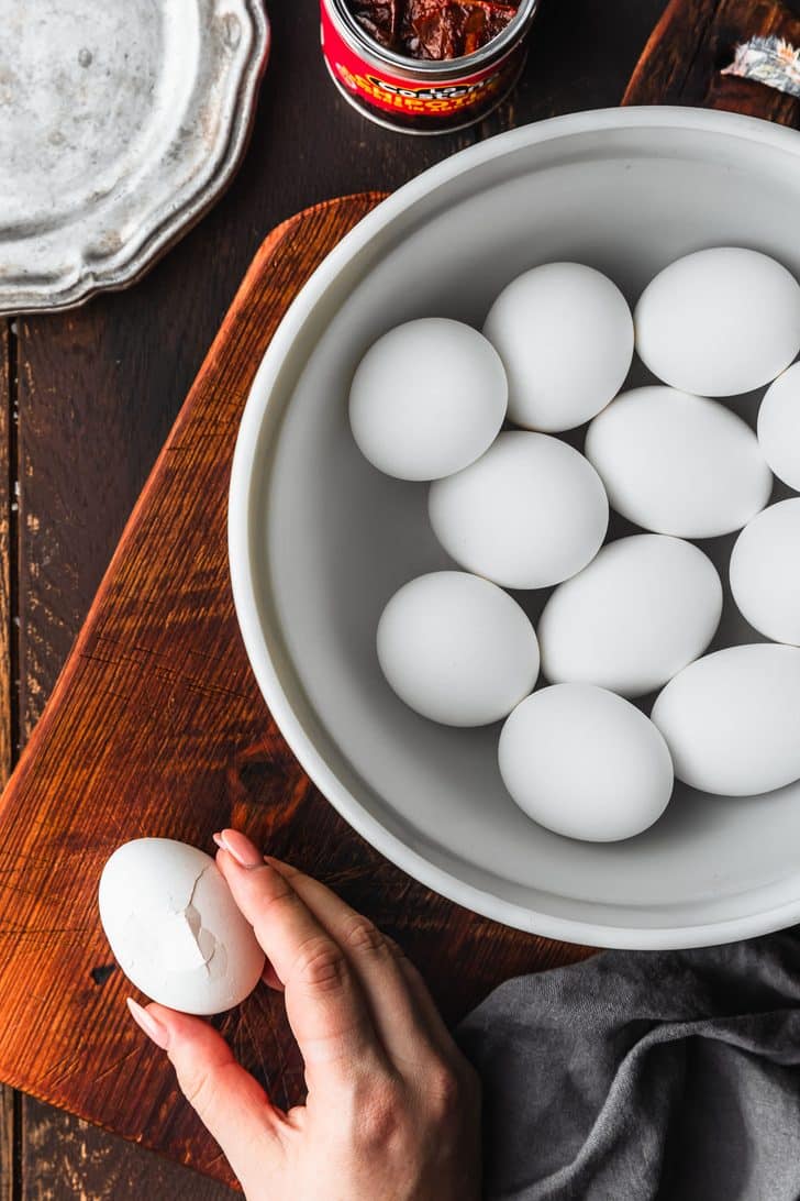 A hand cracking an egg on a wood board.