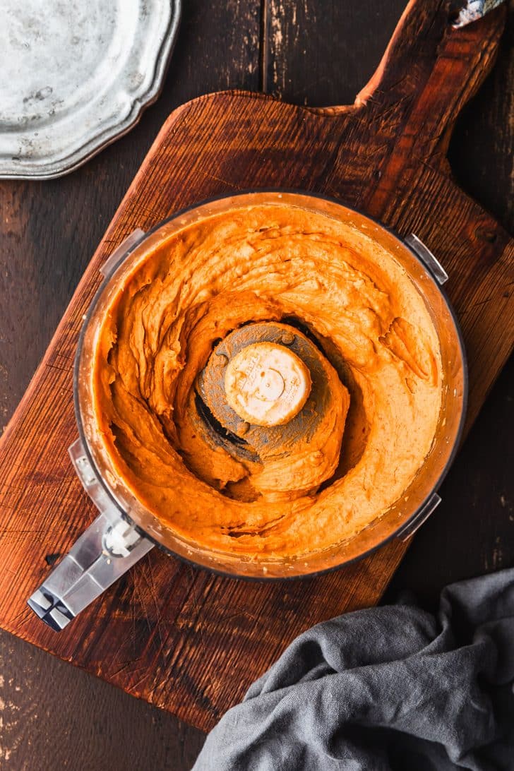 A food processor bowl with filling for Halloween deviled eggs on a wooden cutting board.
