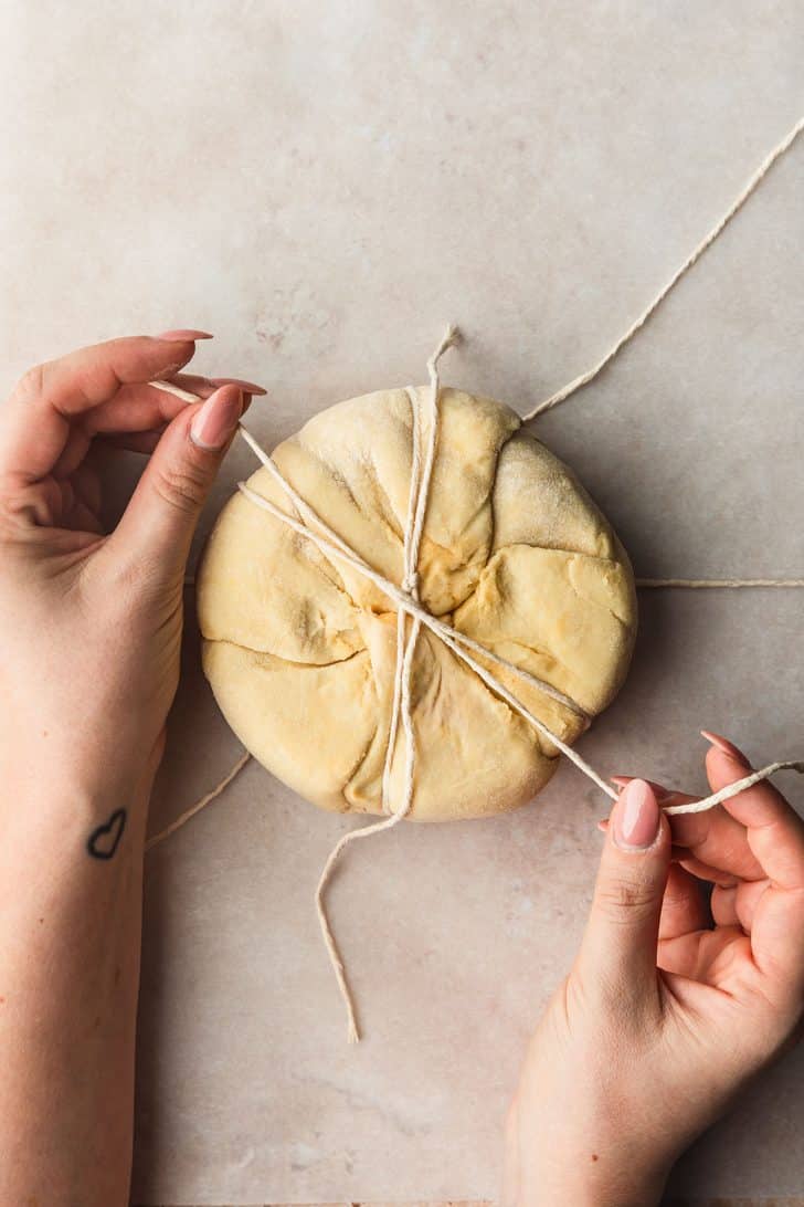 Hands using twine to create a pumpkin shaped baked brie.