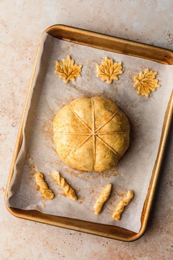 A gold sheet pan with a raw pumpkin-shaped baked brie.