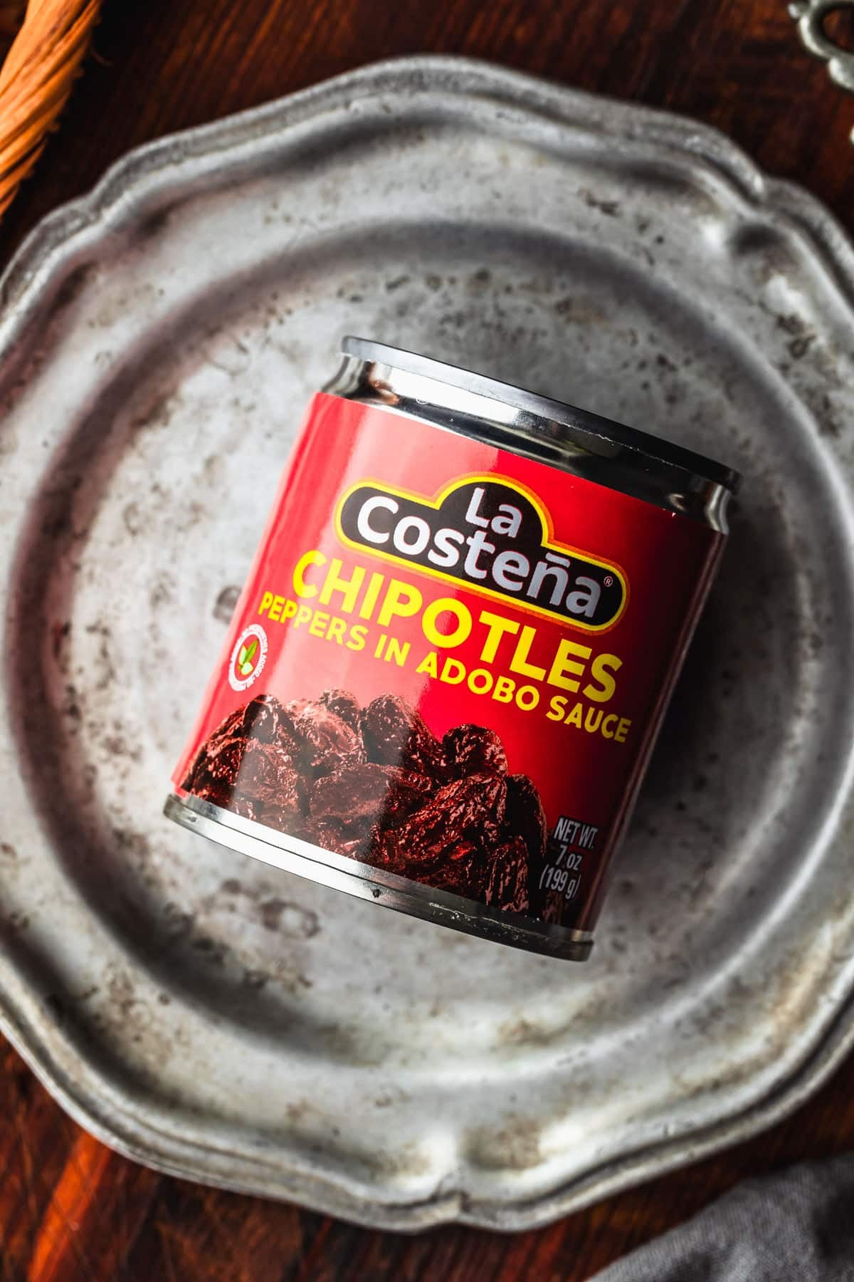 A can of chipotle peppers on a silver platter on a wood table.